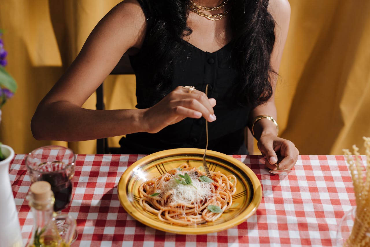 Close-up of a woman twirling spaghetti bolognese on a dining table.