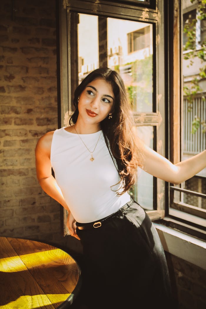 Stylish woman in sunlit room by large window, exuding confidence and warmth.